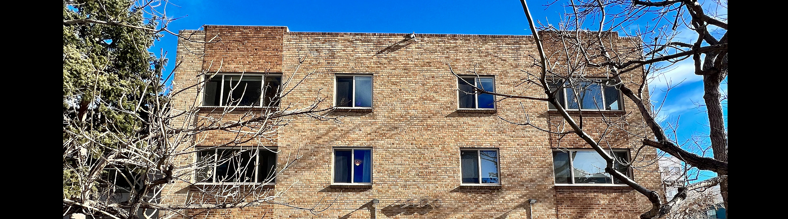 Front view of a three-story brick apartment building with multiple windows and a fenced entry.