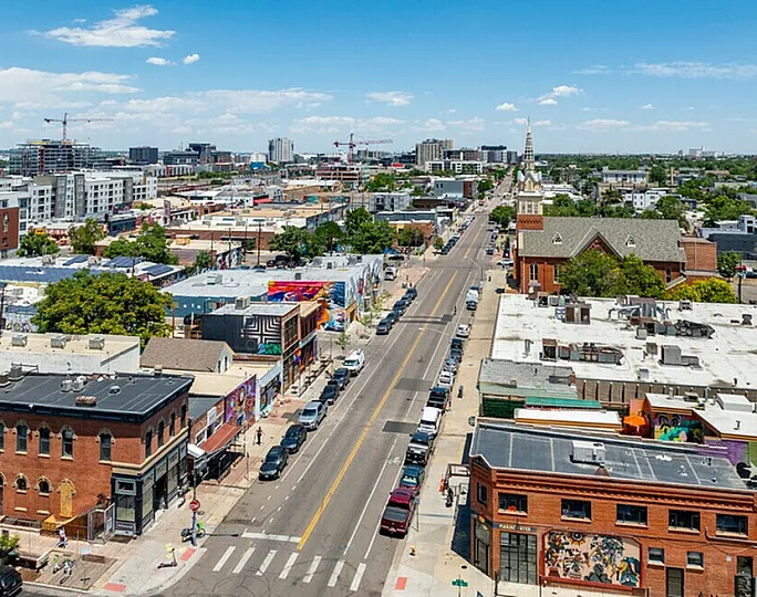 Aerial view of a bustling urban neighborhood with colorful buildings, tree-lined streets, and a skyline adorned with cranes.