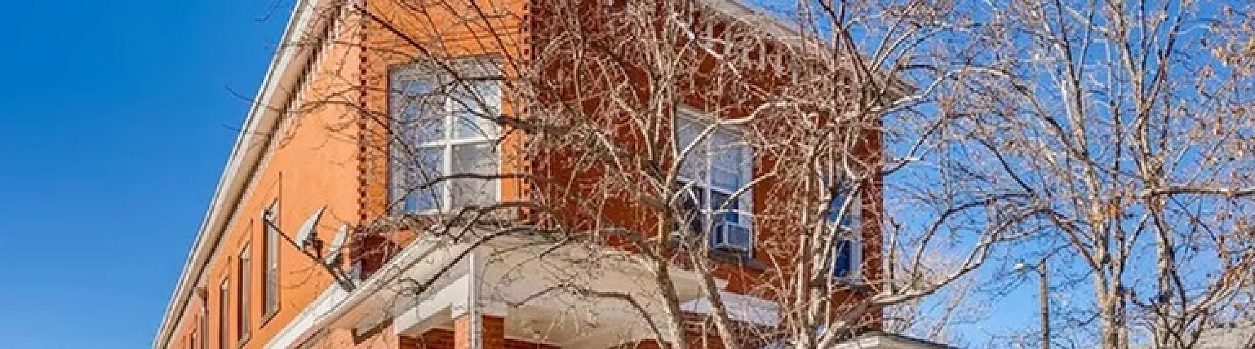 Classic red brick apartment building on a sunny day, showcasing traditional architecture and a welcoming front porch.