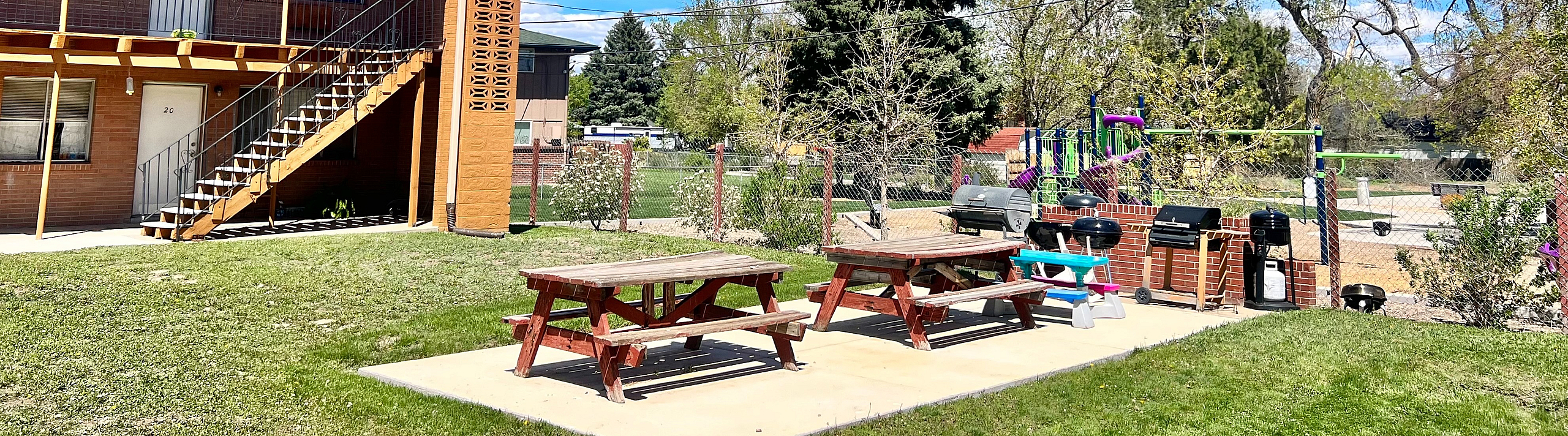 Charming apartment complex with outdoor picnic area and playground under a bright blue sky.