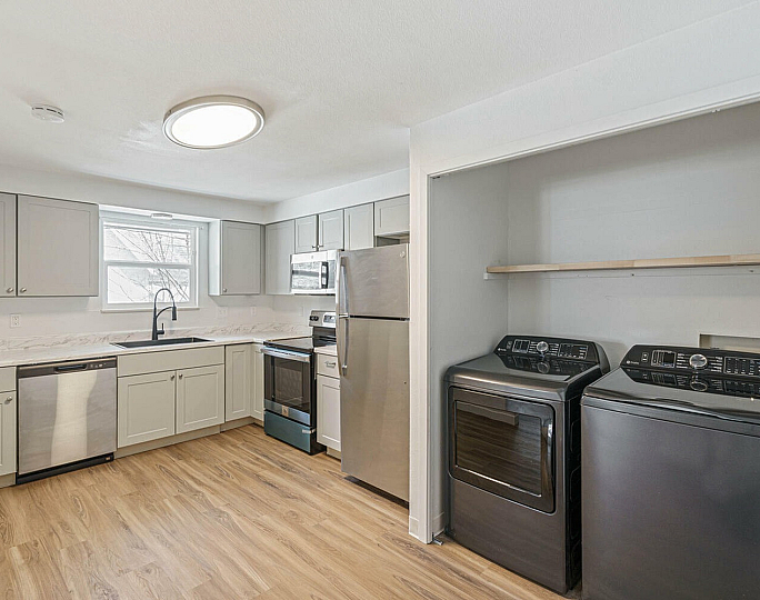 Modern kitchen with stainless steel appliances, elegant wood flooring, and convenient in-unit washer and dryer.