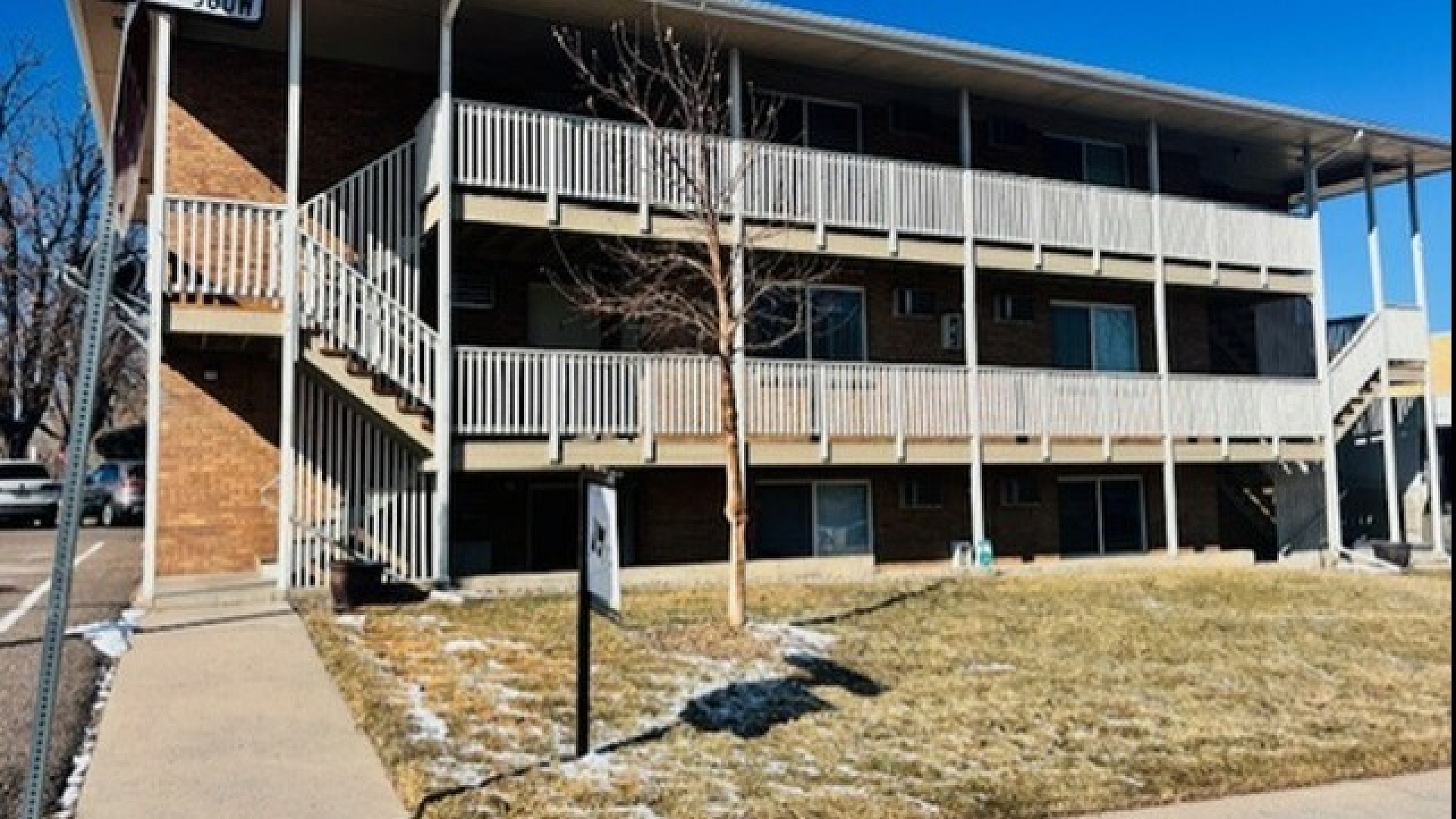 Charming mid-century apartment building with private balconies, surrounded by a well-maintained lawn and clear blue skies, situated at the corner of a quiet street.