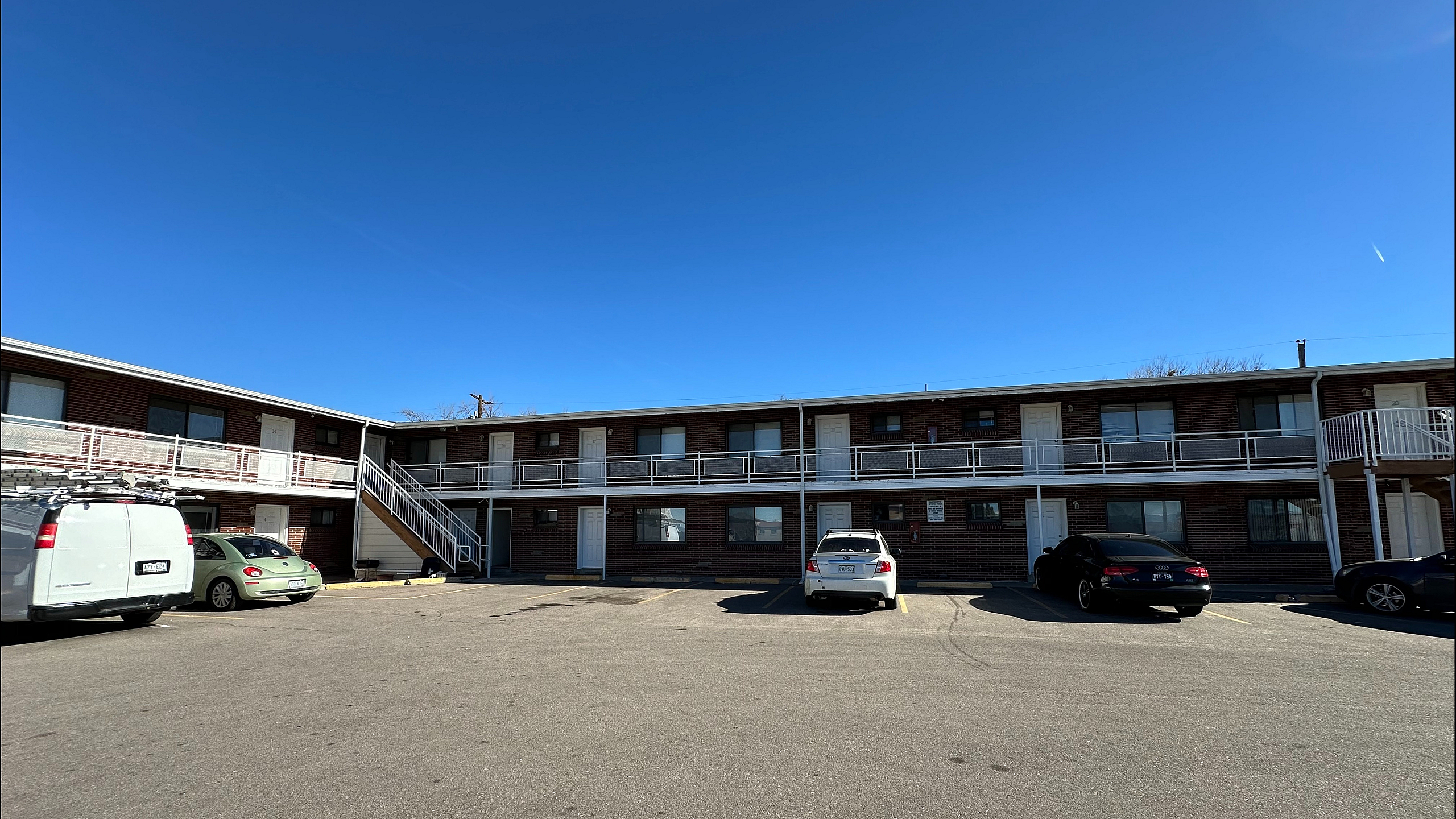 Inviting two-story apartment complex with modern railing design, ample parking, and clear blue skies.