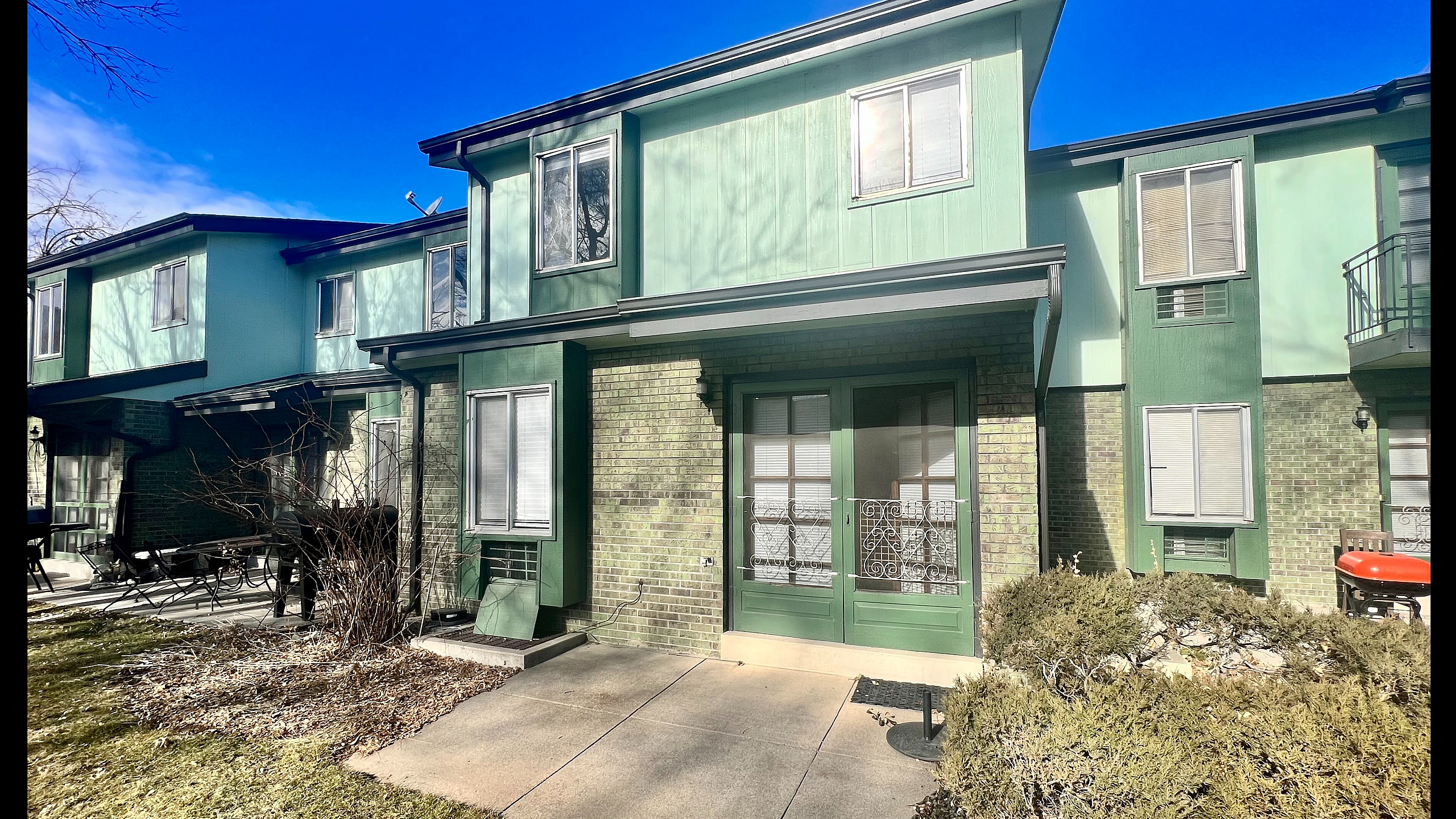 Charming two-story green townhouse with modern features, large windows, and inviting patio in a serene neighborhood setting.