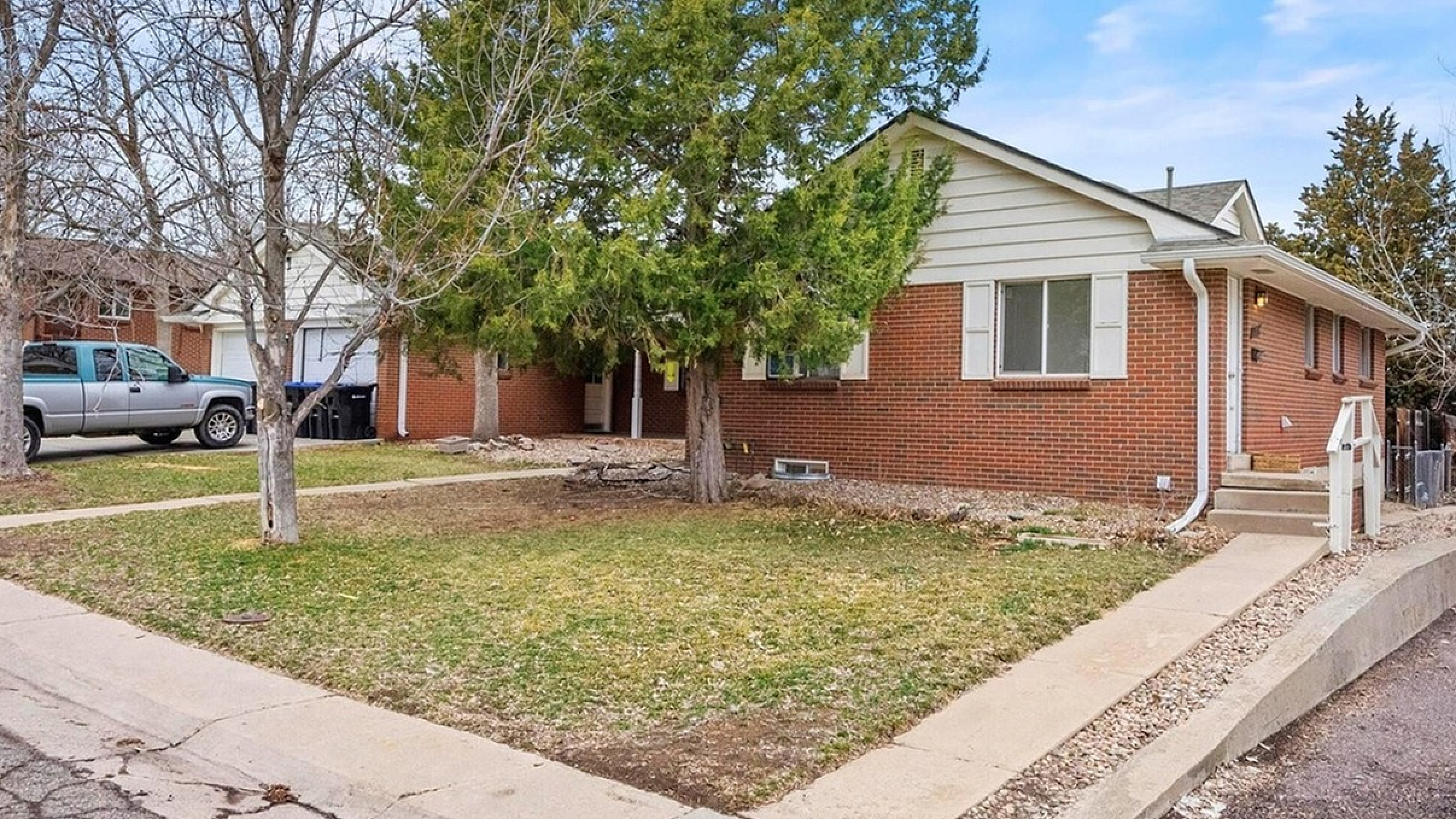 Charming single-story brick home with a lush front yard, mature trees, and inviting walkway, perfect for family living.