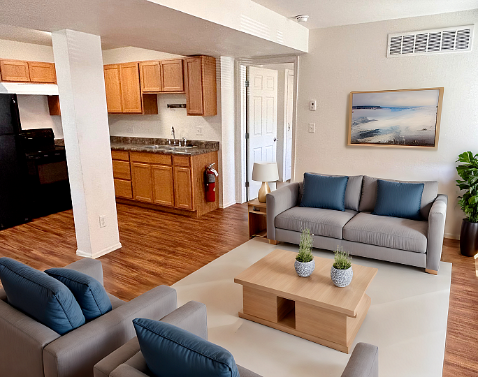 Inviting open-concept living space featuring a modern kitchen with wooden cabinets, cozy seating with plush blue cushions, and elegant wood flooring.