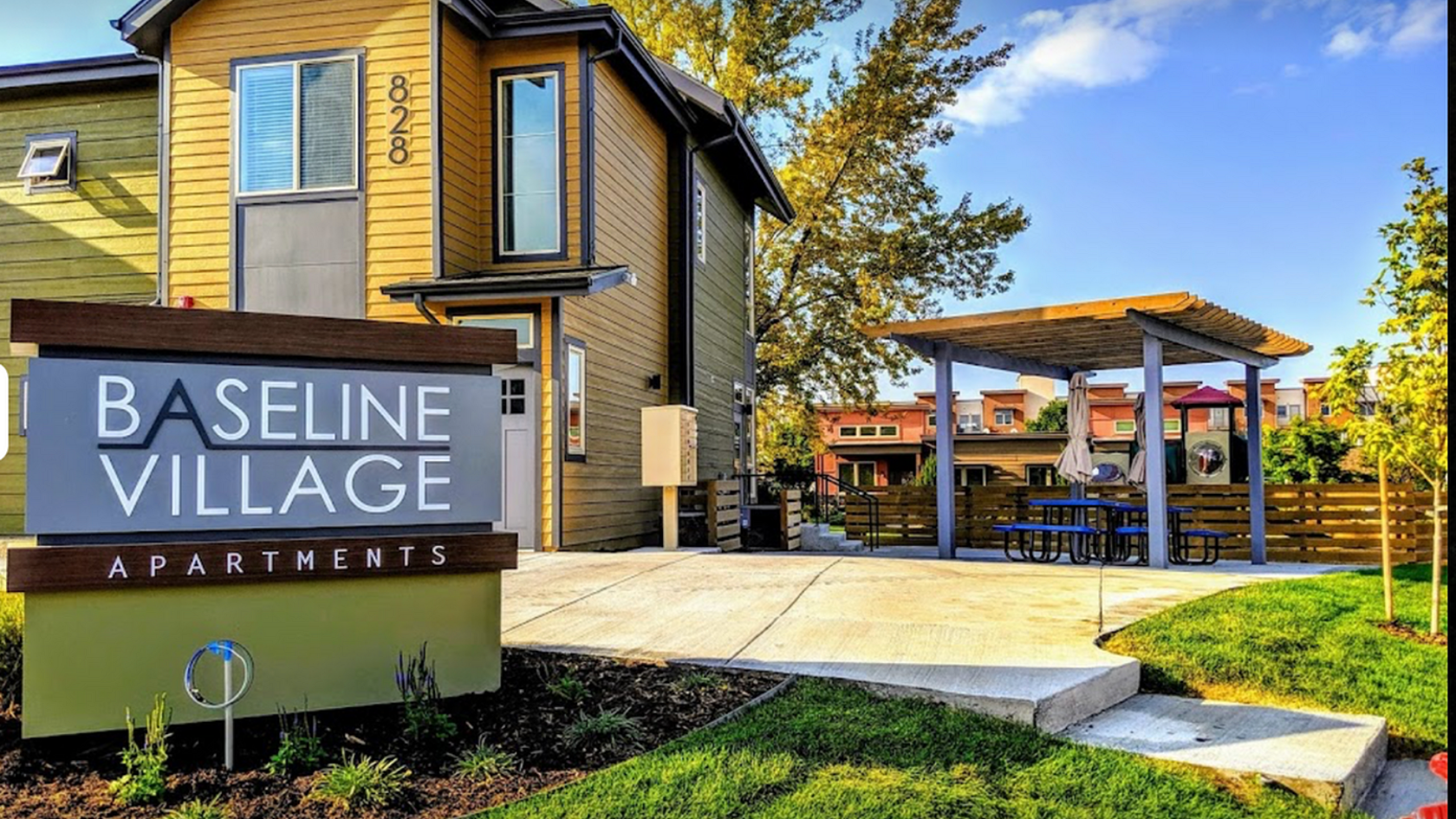 Charming Baseline Village Apartments exterior with modern architecture, lush landscaping, and inviting outdoor seating area under a stylish pergola.