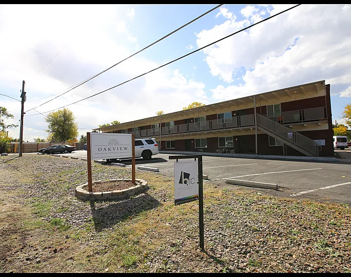 Sunny day view of Oakview Apartments showcasing a two-story building with spacious parking and lush greenery.
