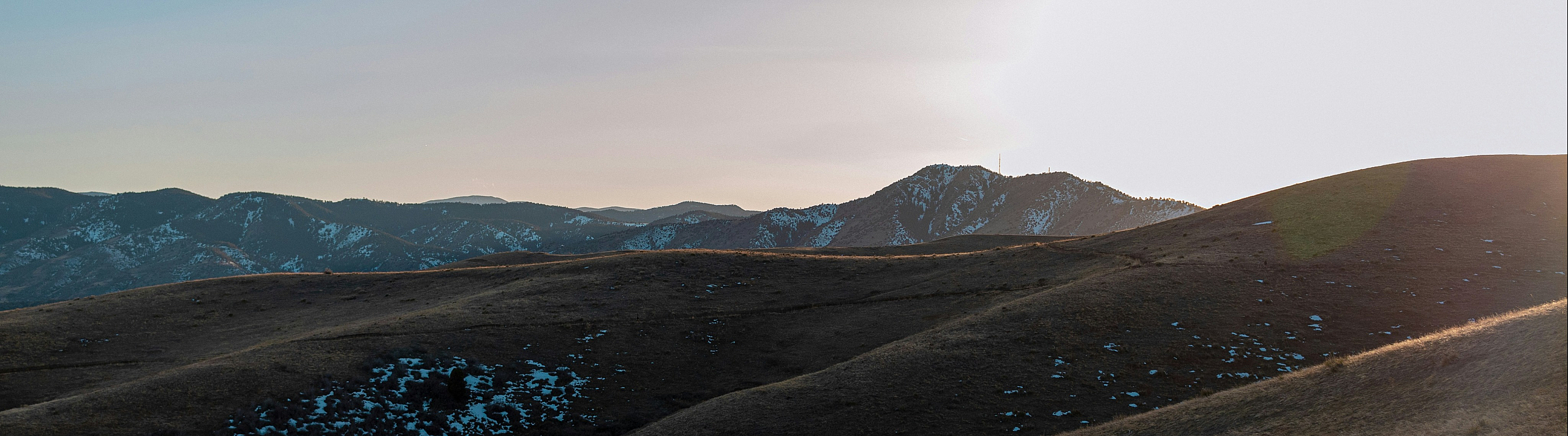 Stunning panoramic view of rolling hills bathed in the golden glow of sunrise with distant snow-capped mountains.