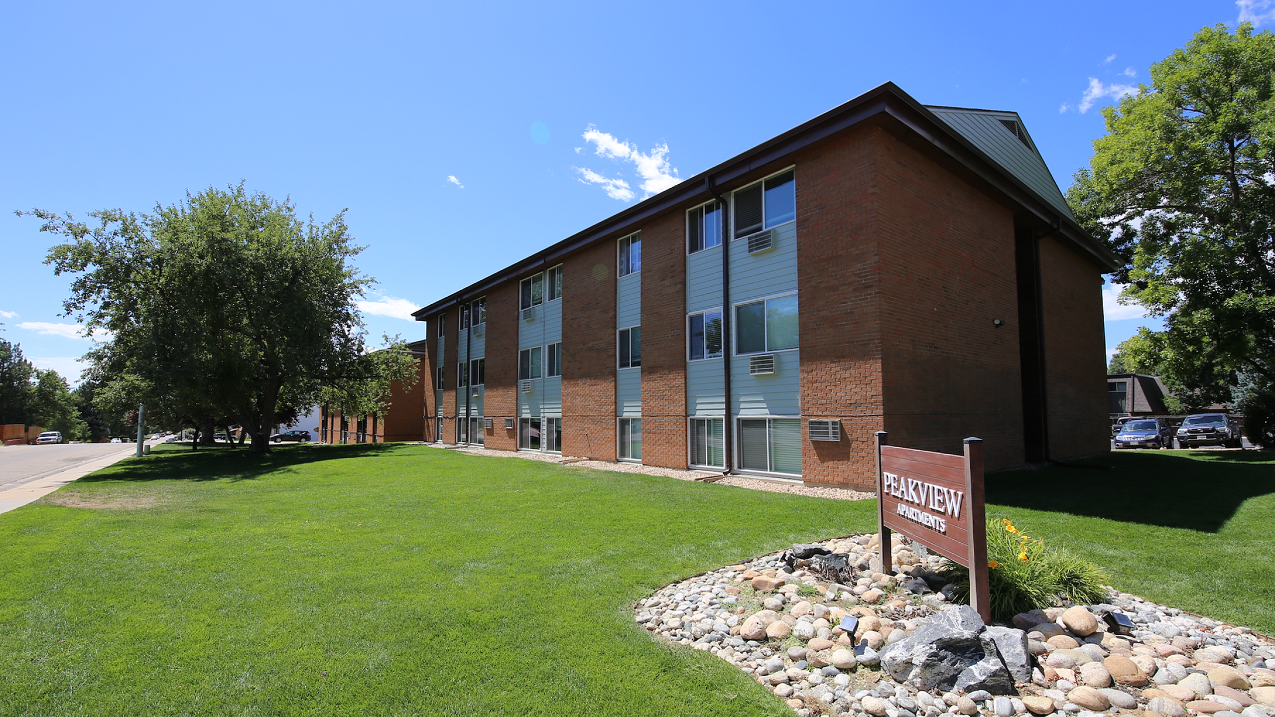 Charming brick apartment building with lush green lawn and vibrant landscape, offering a serene living environment at Peakview Apartments.