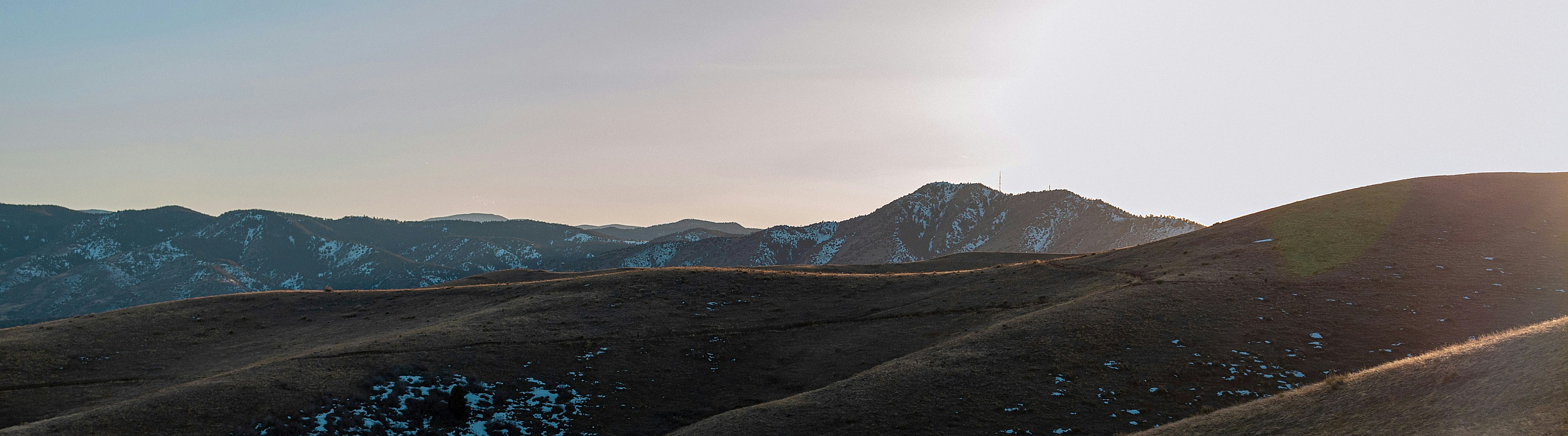 Serene landscape with rolling hills bathed in golden sunlight against a backdrop of distant mountains and a clear sky.