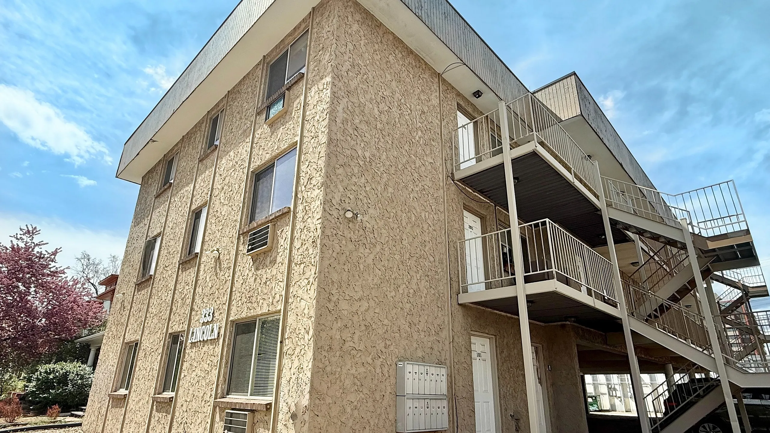 Charming exterior view of a multi-story apartment building with textured walls and outdoor staircases, set against a scenic sky.