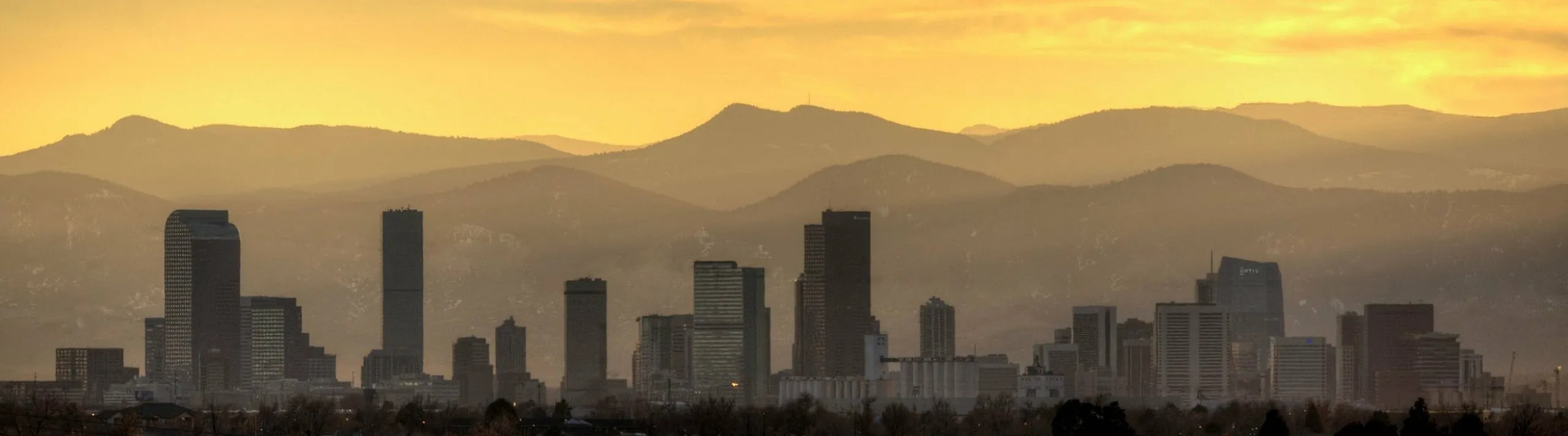 Stunning city skyline silhouette against a dramatic sunset with majestic mountains in the background.