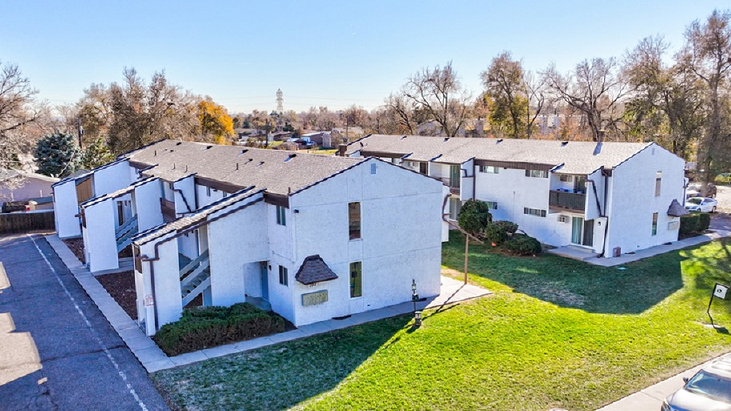 Charming apartment complex with modern architecture, surrounded by lush greenery and spacious parking area.