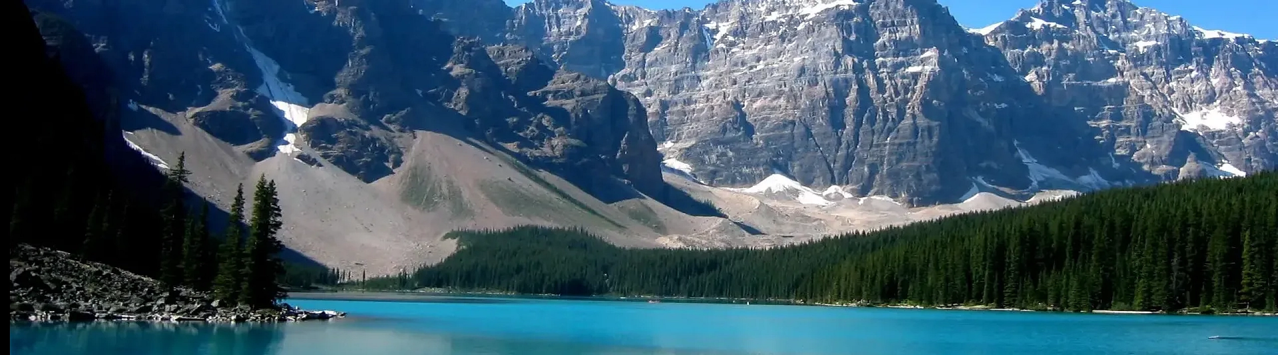 Scenic mountain road leading through lush green forest with majestic snow-capped peaks in the background.