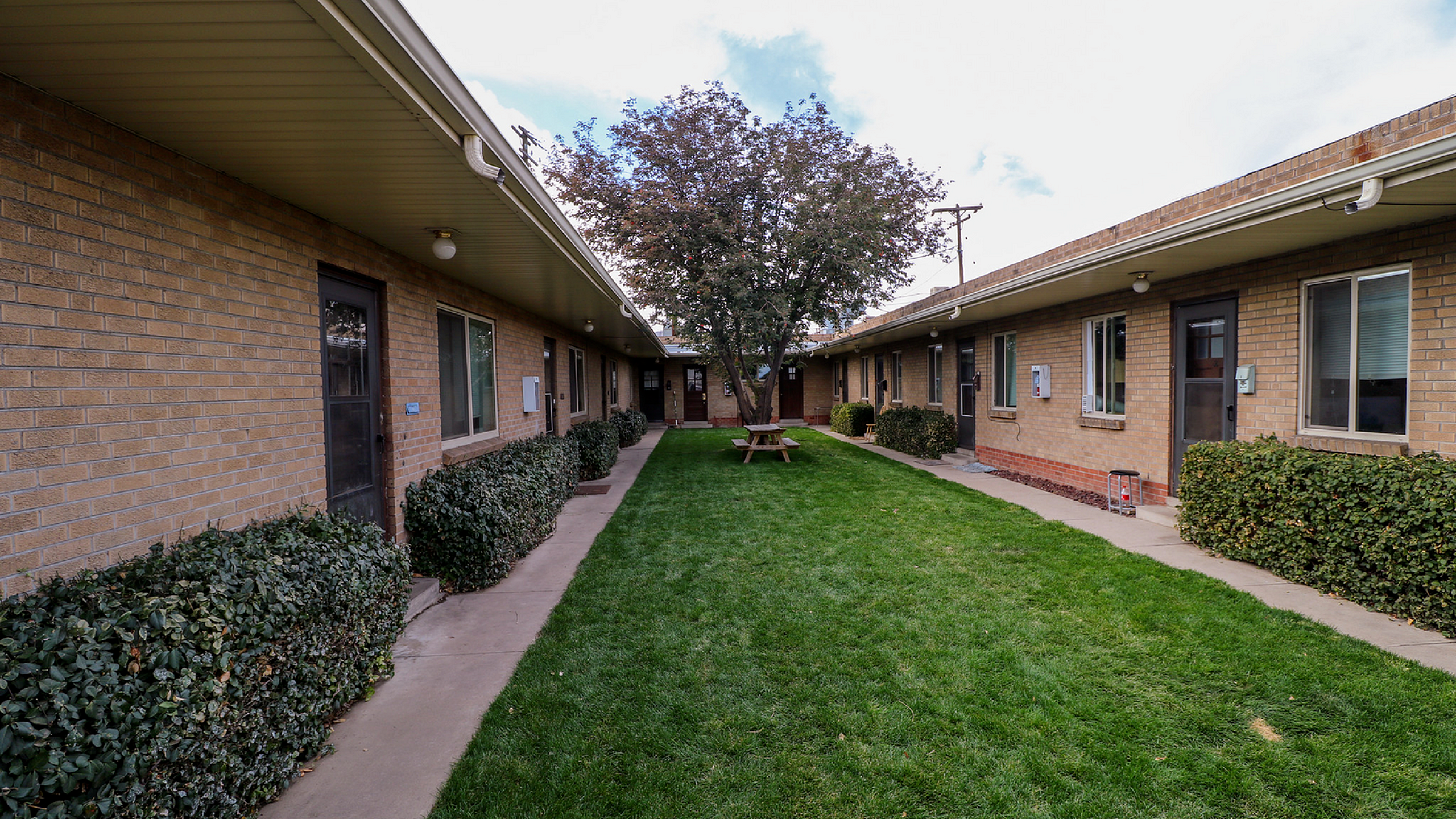 Charming courtyard of a brick apartment complex featuring lush green grass, picnic tables, and well-maintained shrubbery.