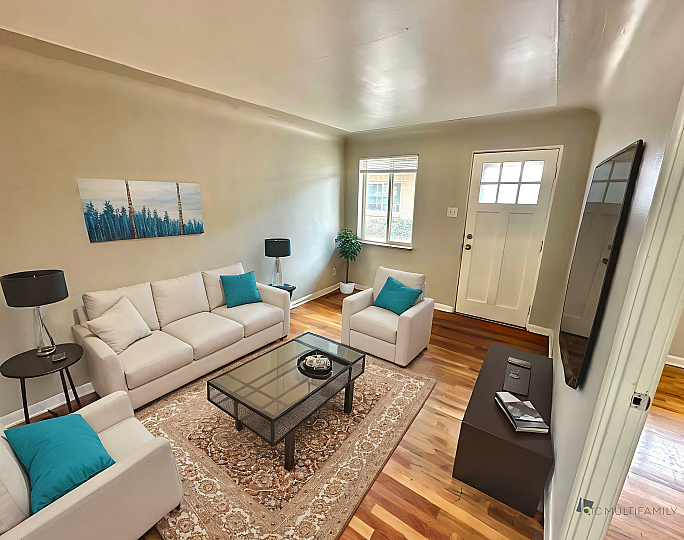 Inviting living room with cozy white couches, colorful teal accents, and sleek hardwood flooring, creating a warm and modern atmosphere.