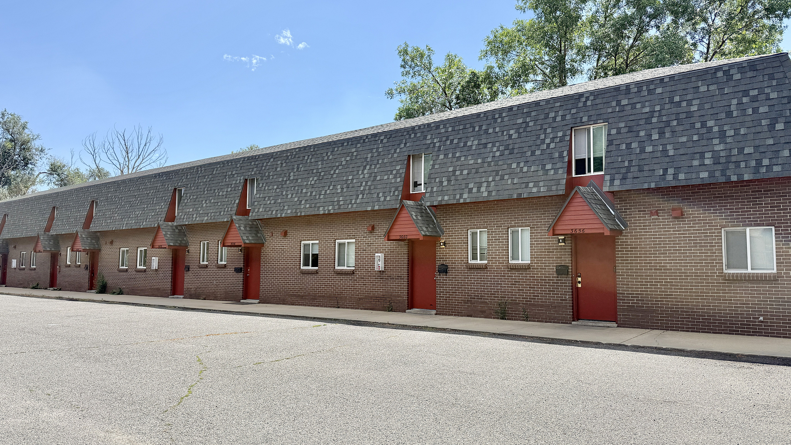 Charming townhouse complex with brick facade, distinctive red accents, and pitched roofline nestled in a serene suburban setting.