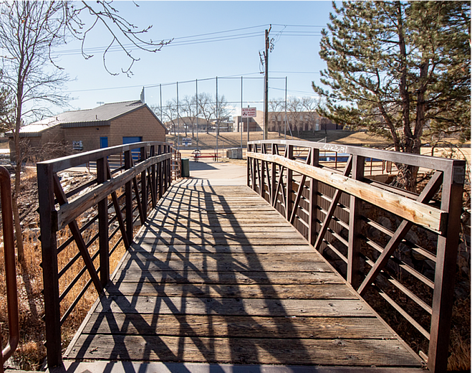 Charming wooden footbridge leading to a serene park setting under a clear blue sky, perfect for outdoor relaxation.