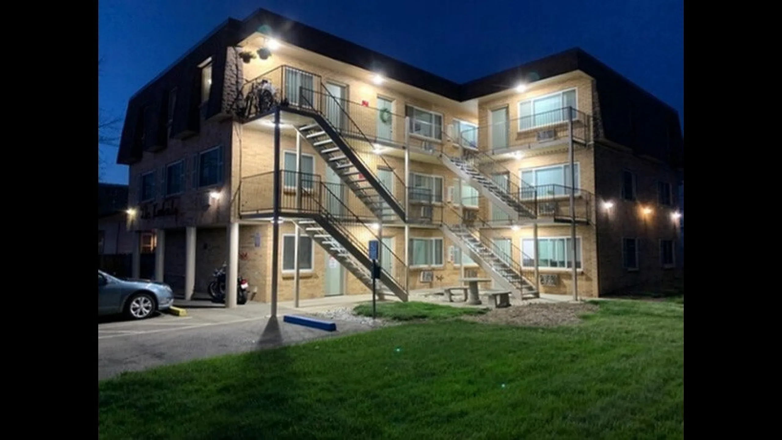 Charming brick apartment building illuminated at night, featuring modern outdoor staircases and inviting balconies, surrounded by greenery.