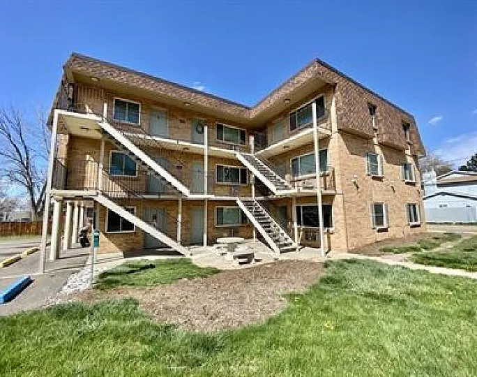 Inviting brick apartment building with lush green lawn on a sunny day, highlighting outdoor staircases and spacious balconies.