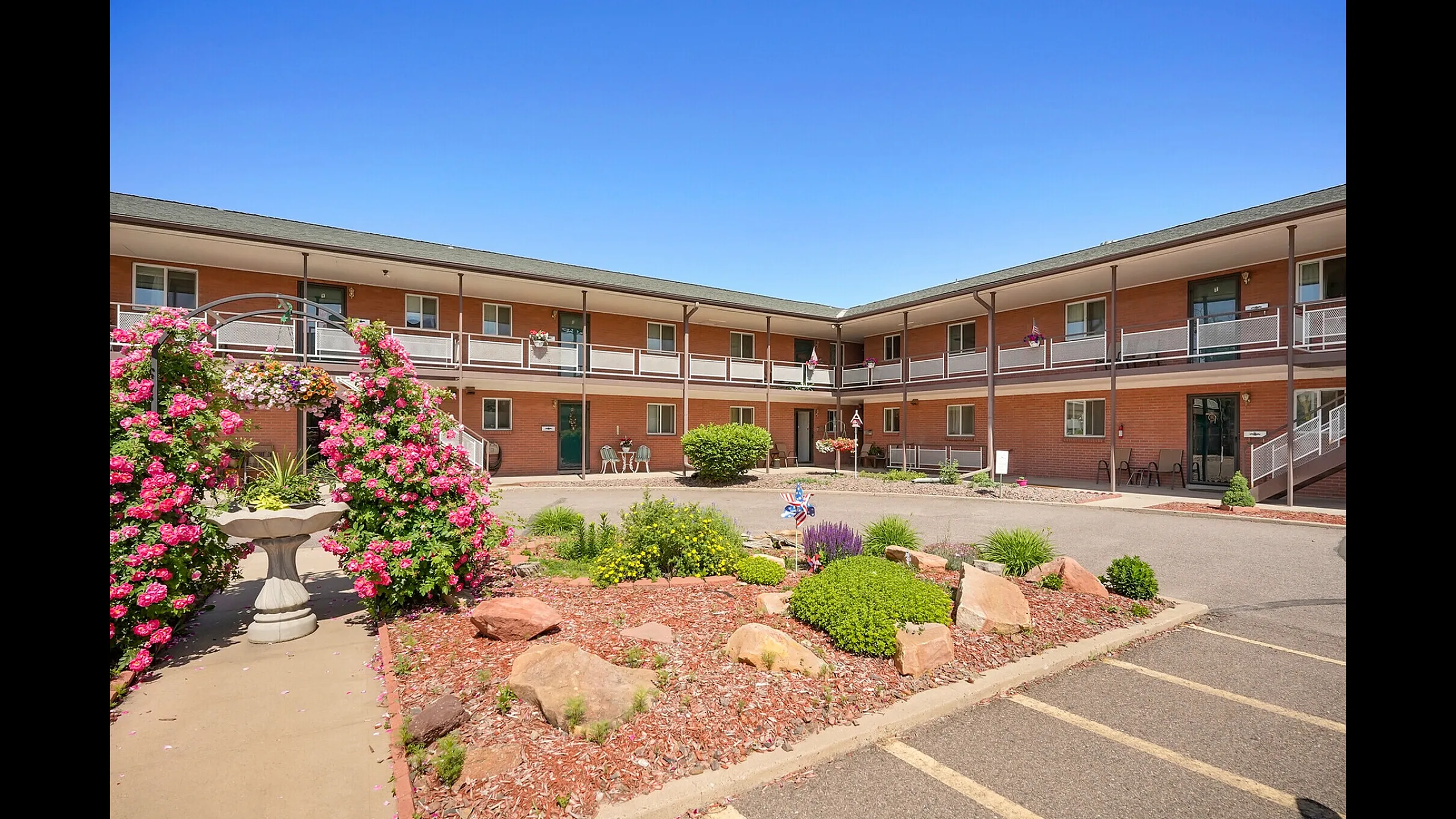 Charming apartment complex courtyard with vibrant flowers, lush greenery, and inviting outdoor seating.