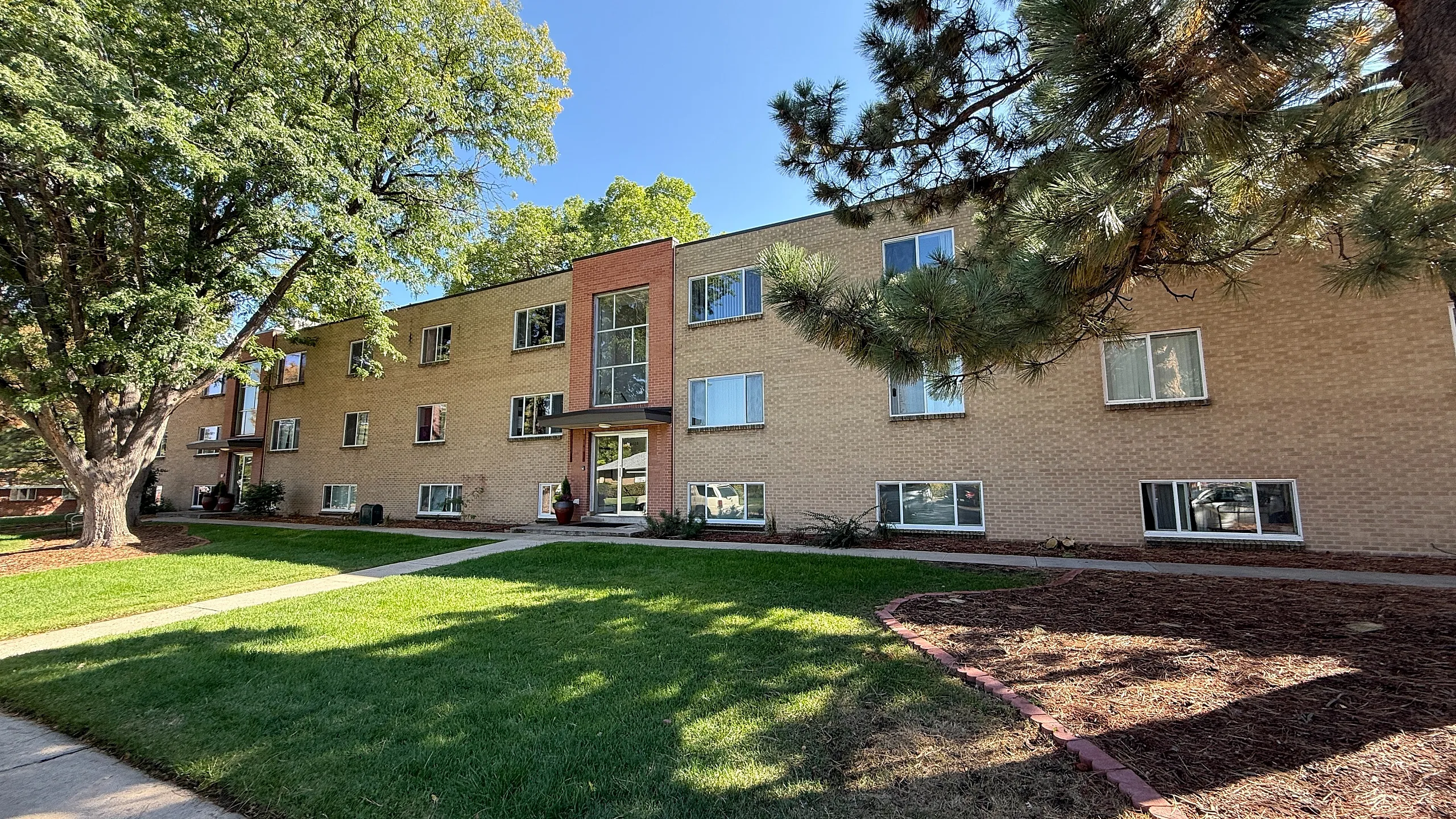 Charming brick apartment building with large windows, nestled in a serene neighborhood with lush green landscaping and mature trees.