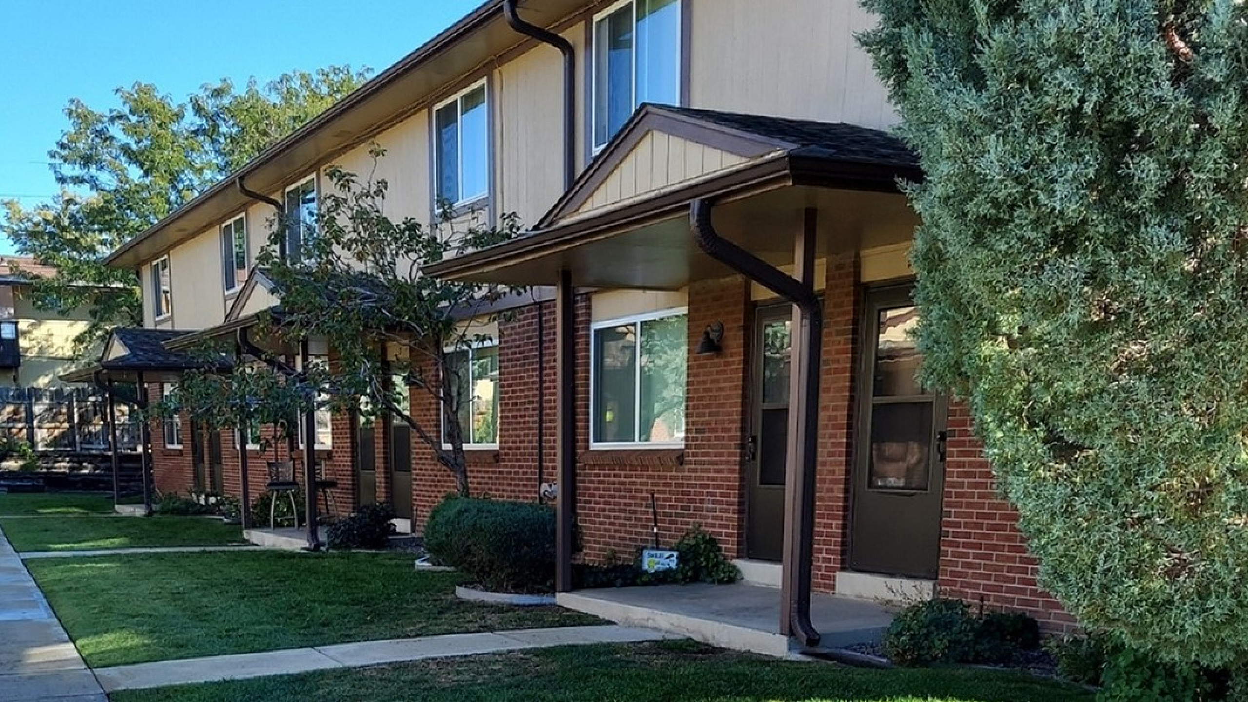 Charming row of townhouses with vibrant brick exterior and lush green landscaping under a clear blue sky.
