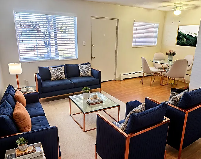 Bright and inviting living room with modern navy sofas, sleek glass coffee table, and a cozy dining area, perfect for entertaining.