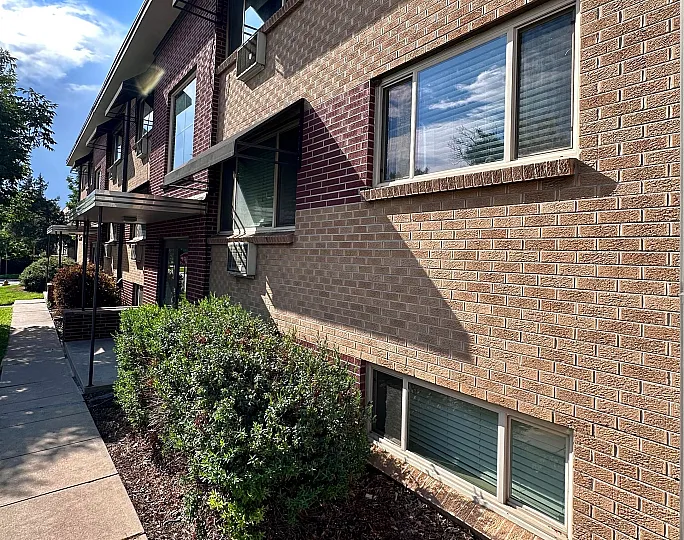 Charming two-story brick apartment building with lush greenery and inviting pathways under a bright blue sky.