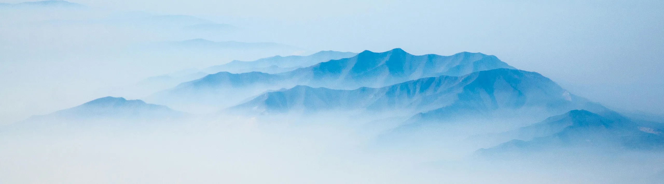 Serene panoramic view of misty blue mountains enveloped in soft morning haze.