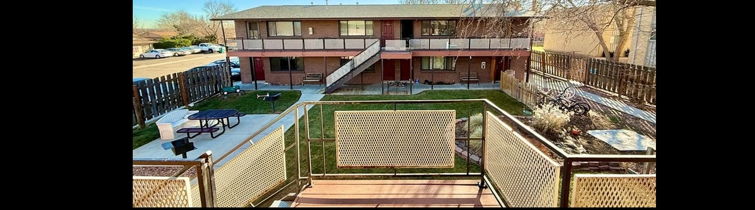 Inviting apartment complex courtyard featuring a charming two-story building, well-maintained garden, and serene outdoor seating area with a sunny daytime ambiance.