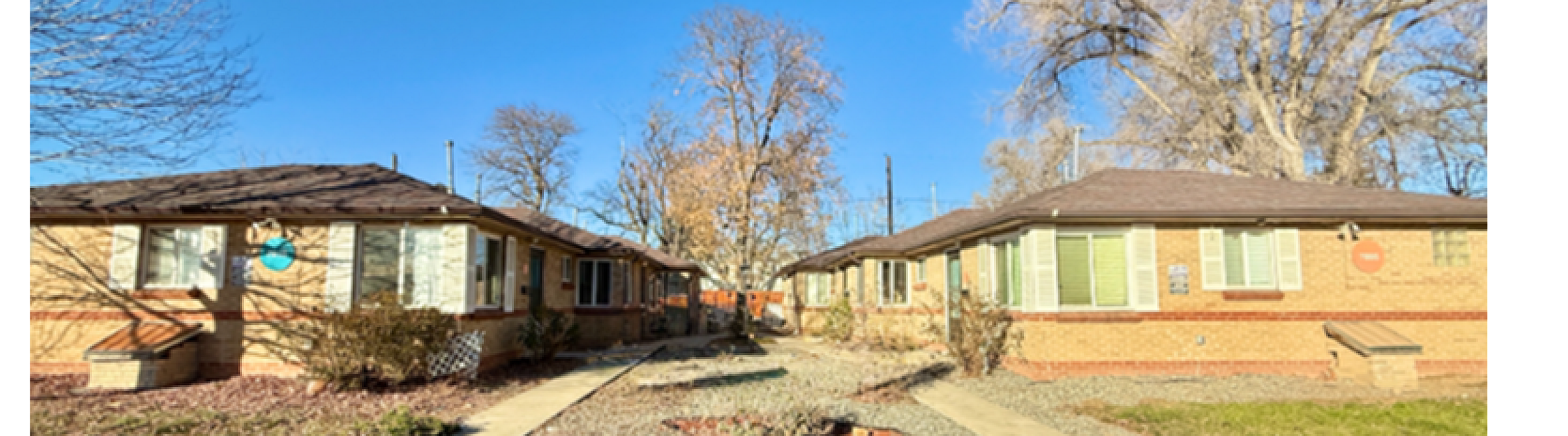 Charming brick apartments with manicured pathways and vibrant autumn trees under a clear blue sky.