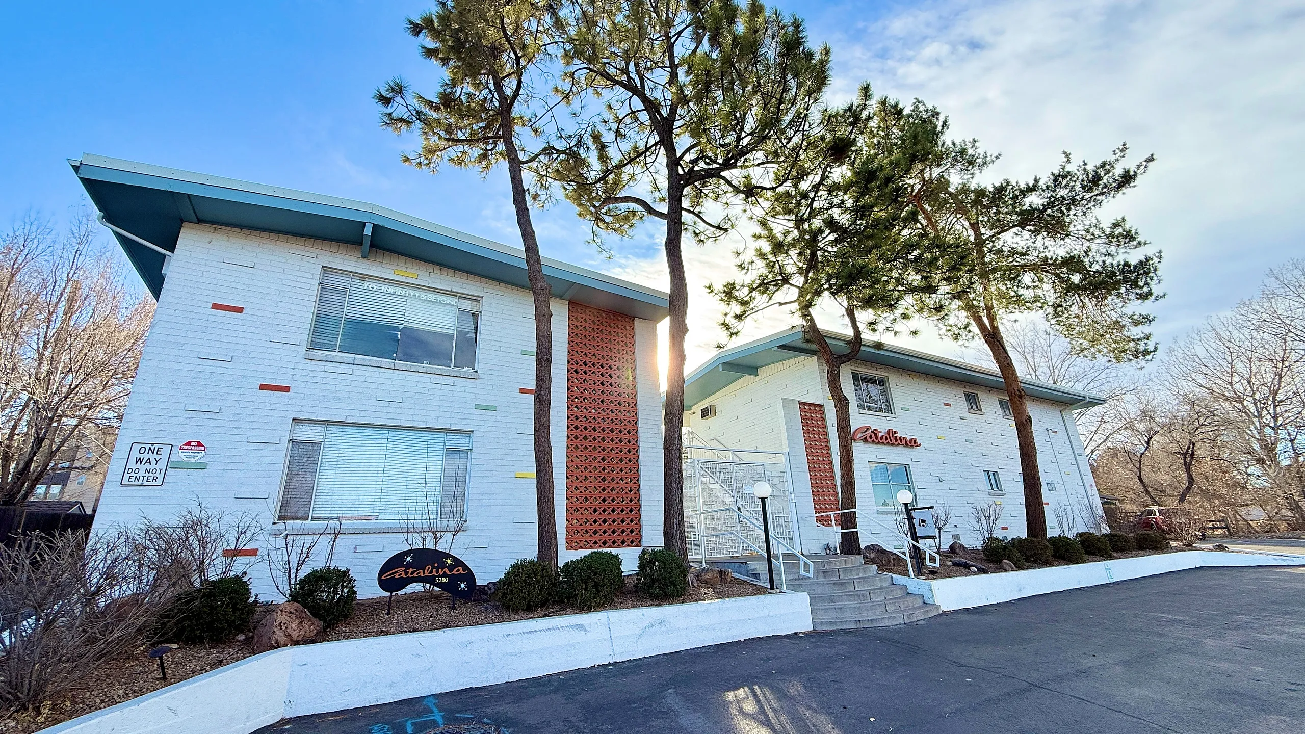 Charming mid-century modern apartment complex with white brick facade, vibrant accents, mature trees, and inviting entryway.