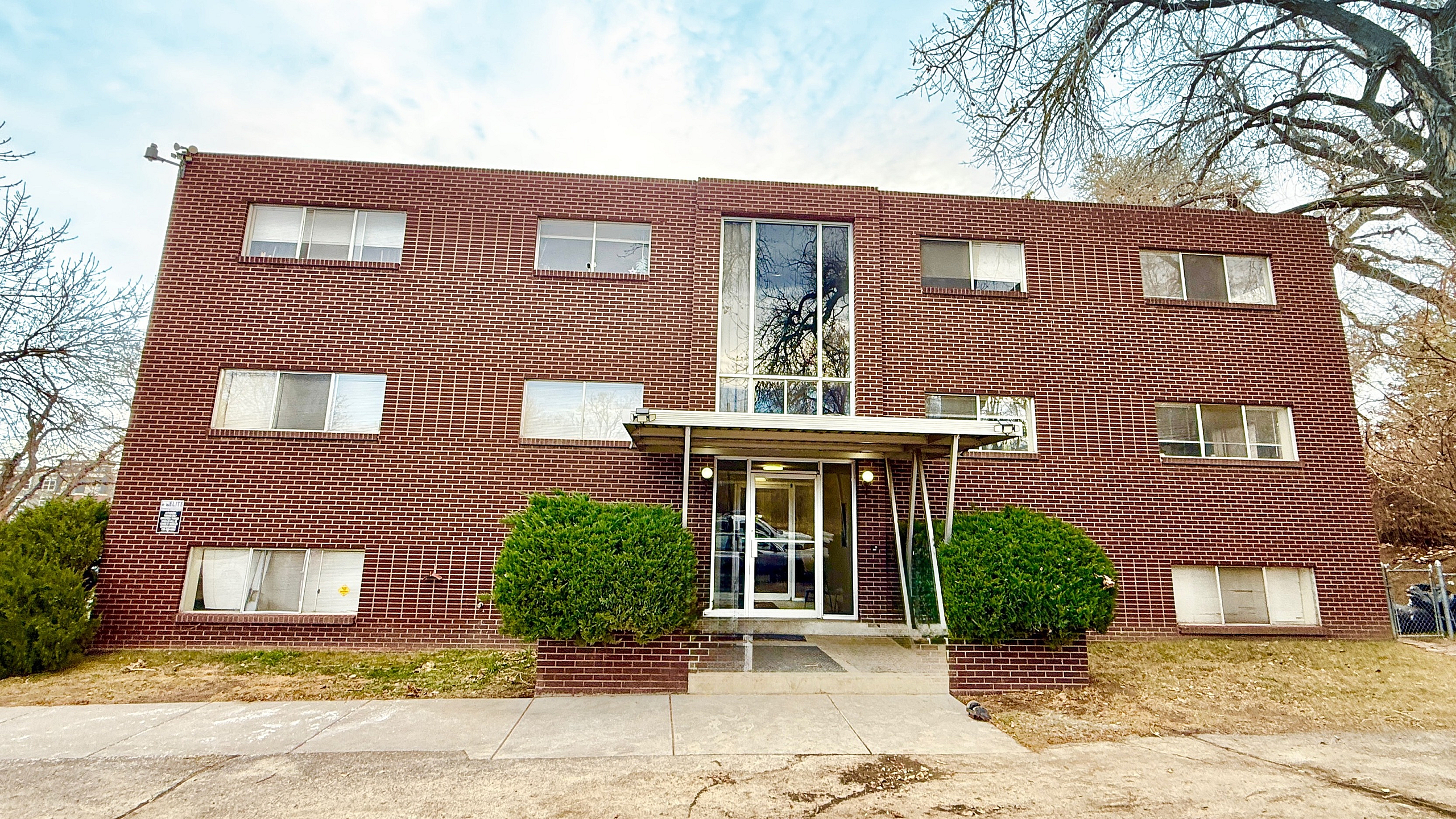 Charming brick apartment building surrounded by lush greenery, offering a cozy and inviting atmosphere.