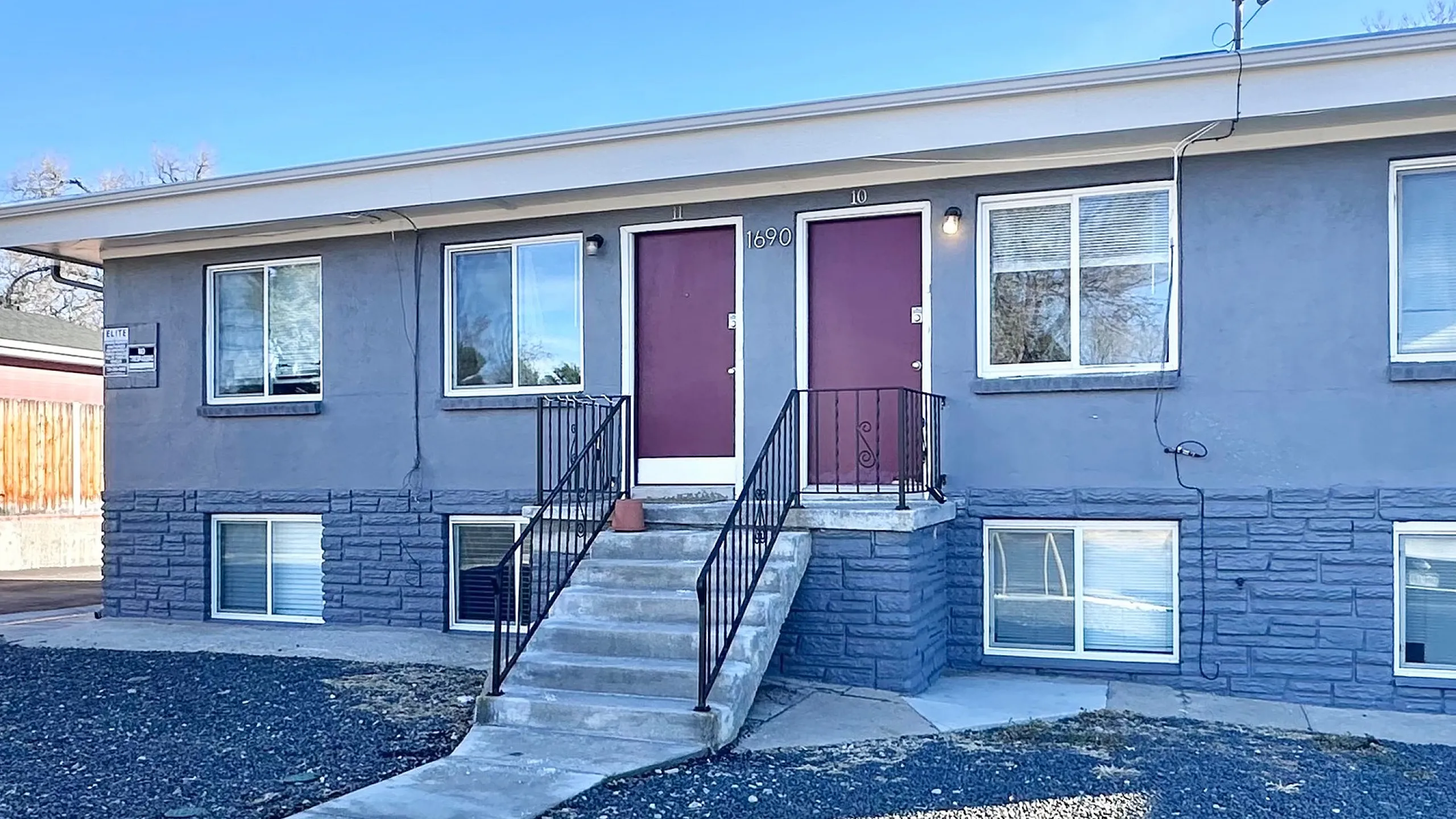 Charming duplex with modern gray exterior and inviting red doors, surrounded by a neat landscape and new leasing opportunities.