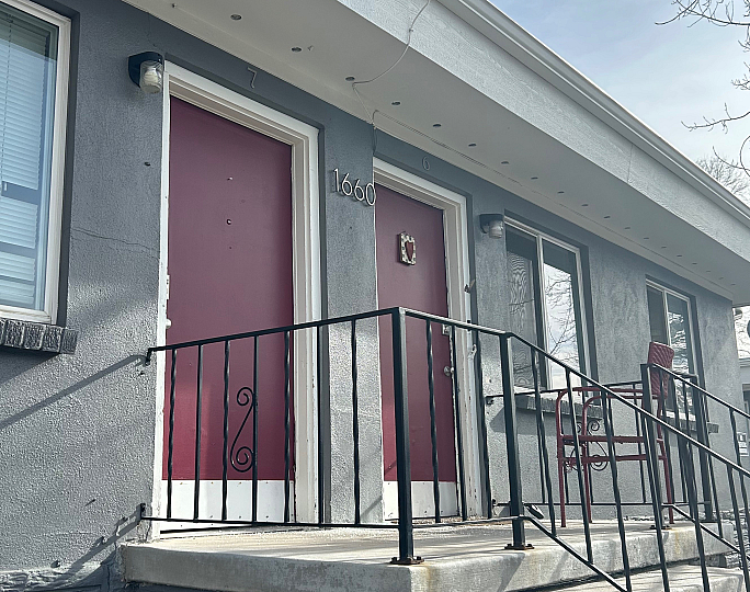 Charming apartment exterior featuring striking red doors, elegant wrought iron railings, and classic stonework under a clear sky.
