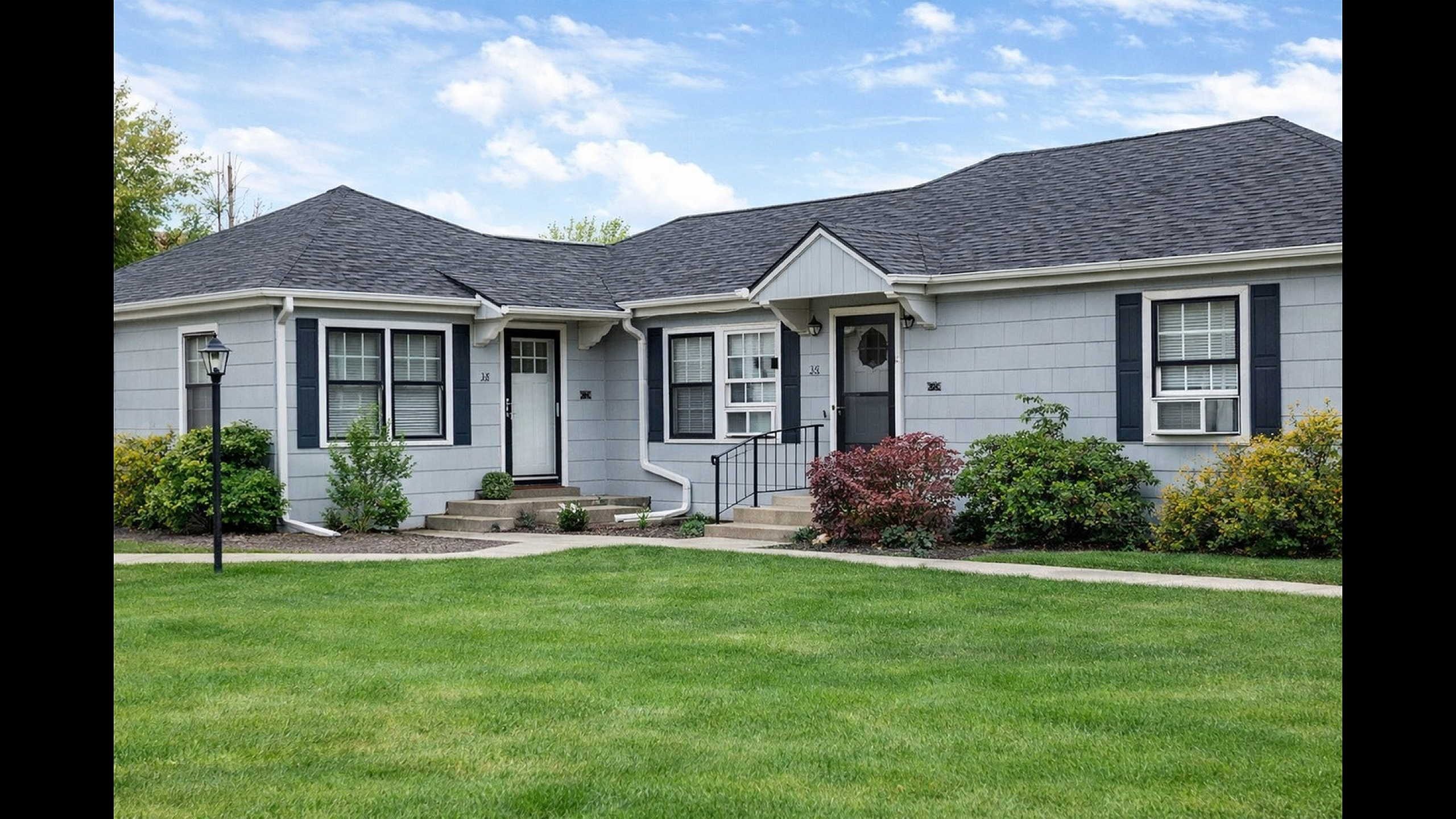 Charming residence with pristine landscaping, featuring a classic gray exterior and welcoming front entry, set against a bright blue sky.