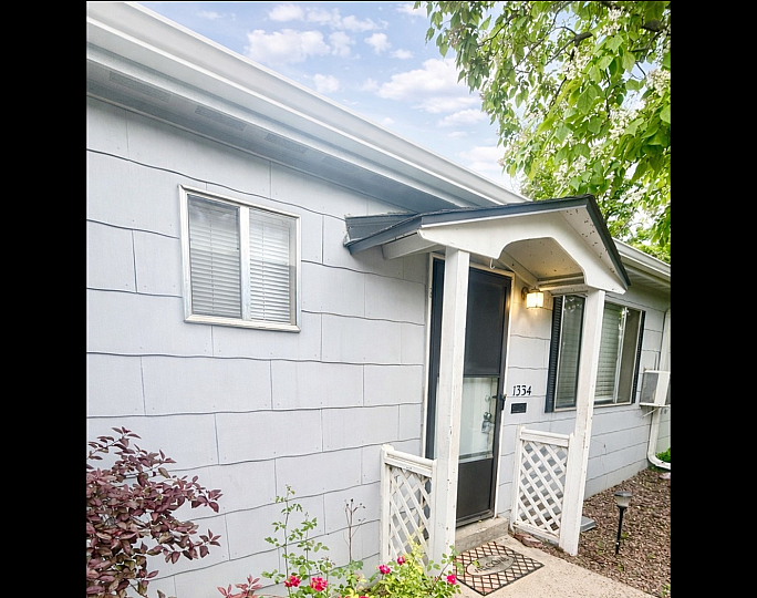 Charming exterior of a cozy home with a welcoming entrance, adorned by vibrant pink flowers and lush greenery.