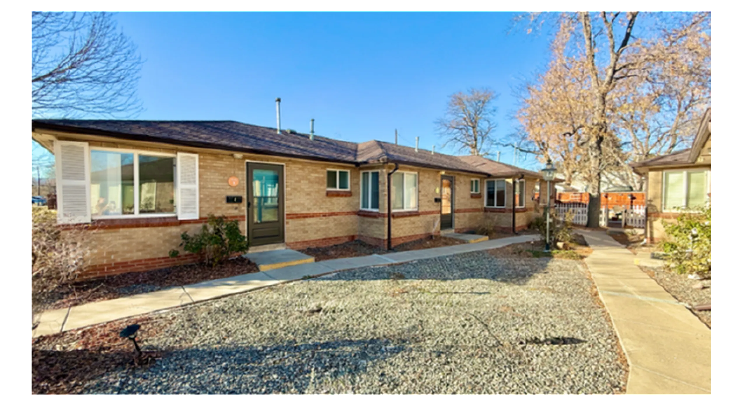Charming single-story brick apartment with large windows, nestled in a quiet neighborhood featuring a well-maintained walkway and mature trees.