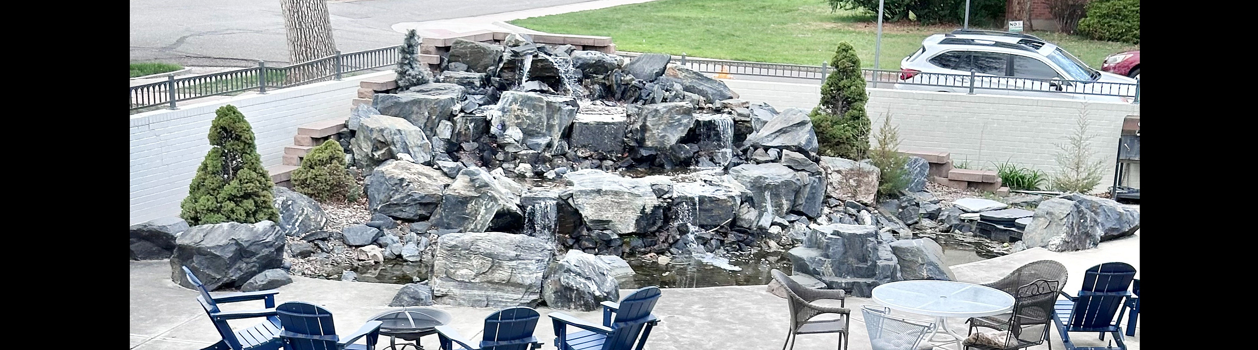 Charming outdoor patio with elegant seating, surrounded by lush greenery and a stunning stone waterfall feature.