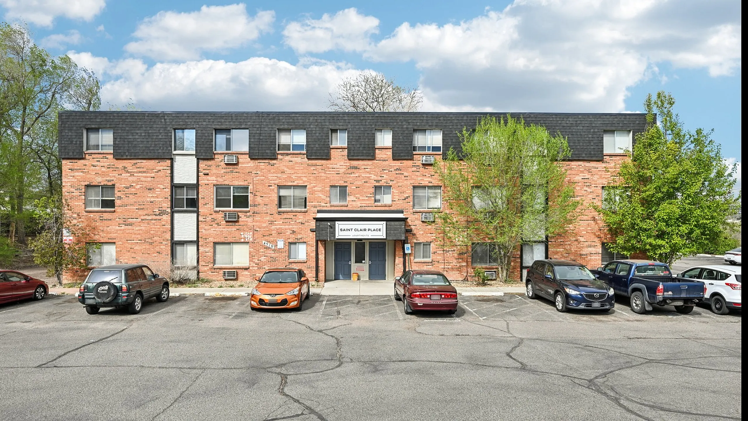 Charming three-story brick apartment building with convenient parking and lush greenery, ideal for comfortable urban living.