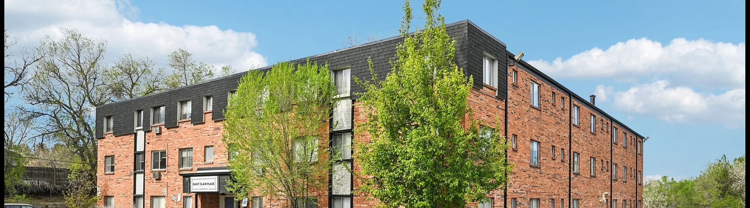 Charming red-brick apartment building with ample parking space, set against a clear blue sky.