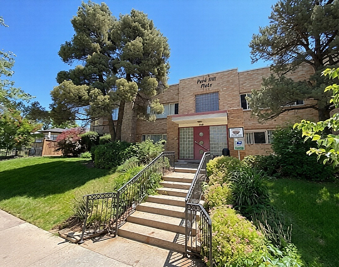 Charming brick apartment building surrounded by lush greenery and vibrant trees, offering inviting curb appeal.