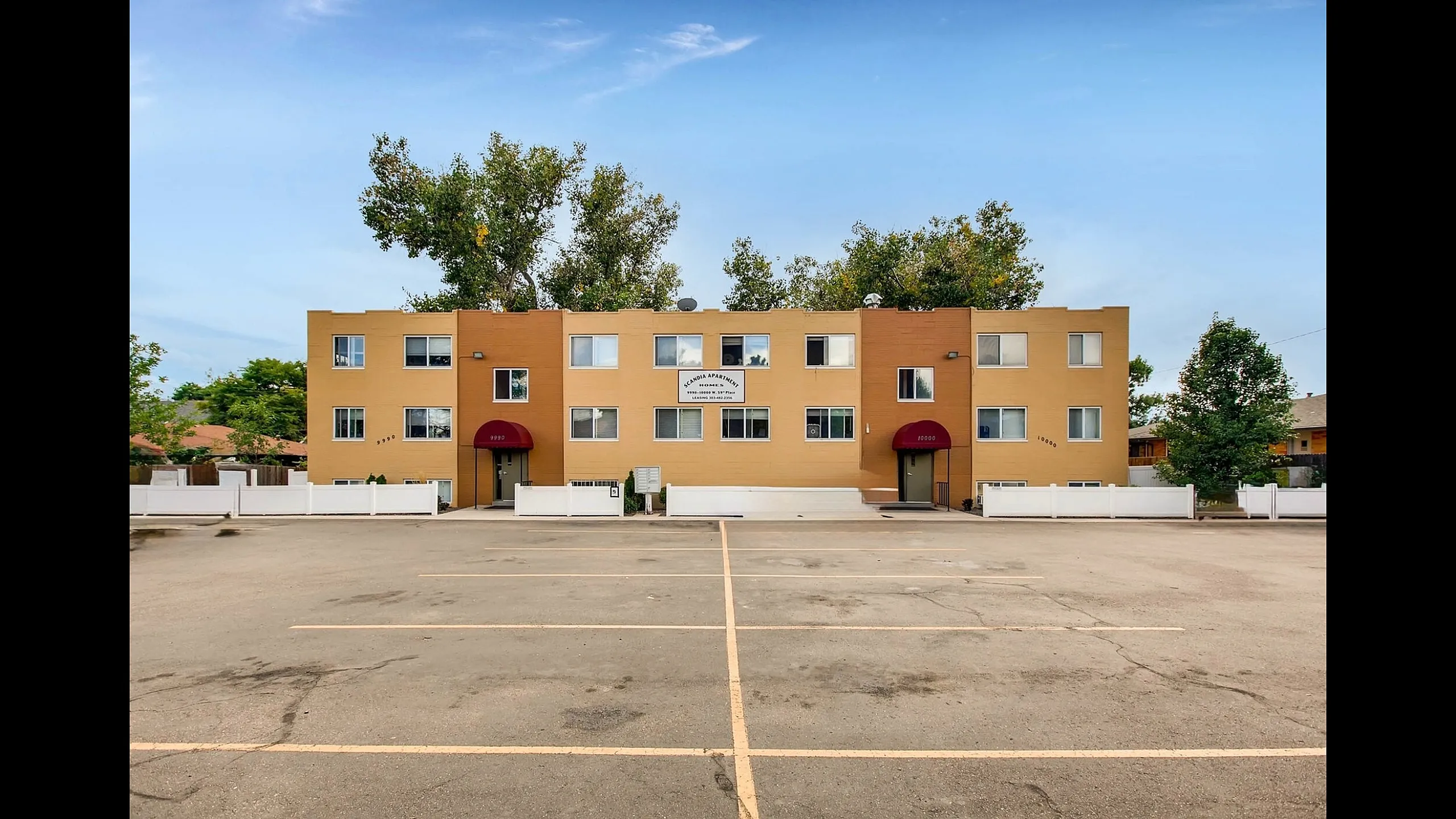 Charming apartment building with red awnings and ample parking, surrounded by lush greenery for a serene living experience.
