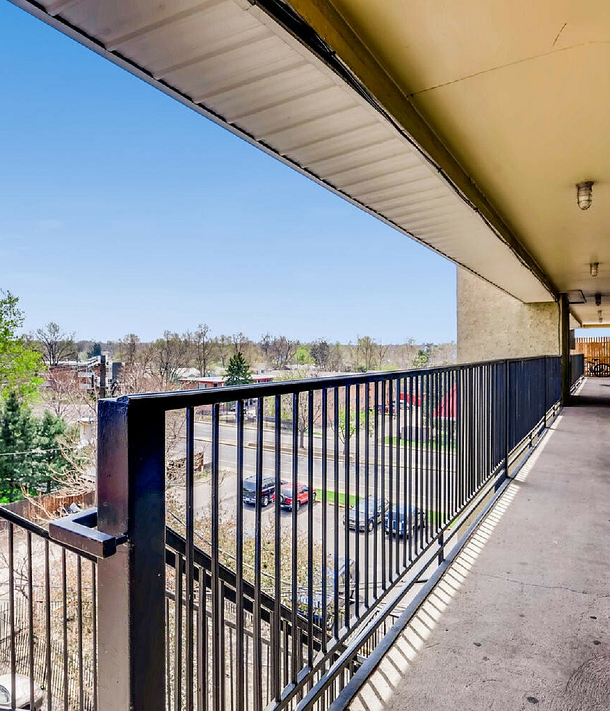 Bright and inviting apartment corridor with a scenic view of lush greenery and a clear blue sky, perfect for enjoying sunny days.