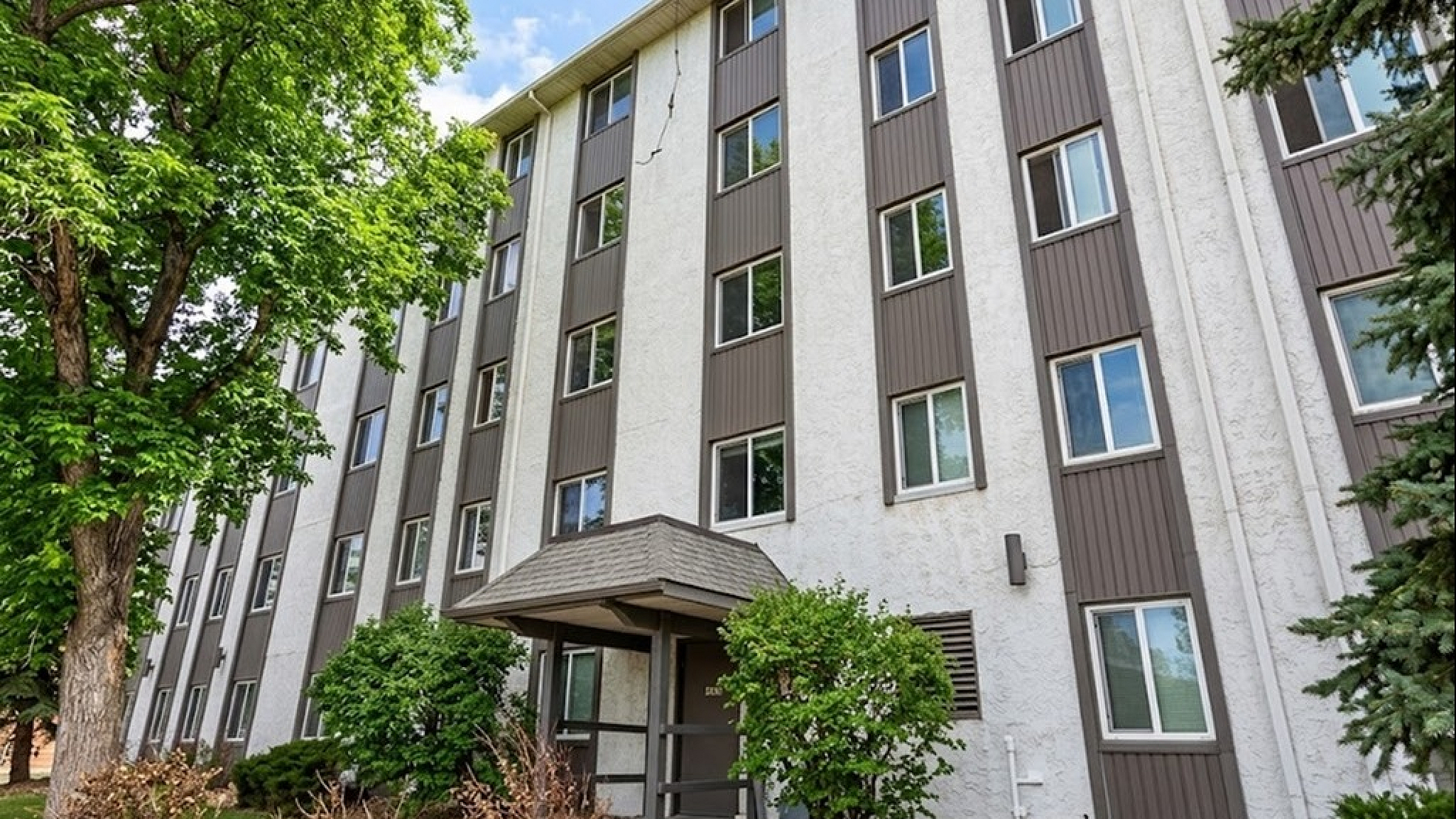 Charming multi-story apartment building with modern design, surrounded by lush greenery and blue skies.