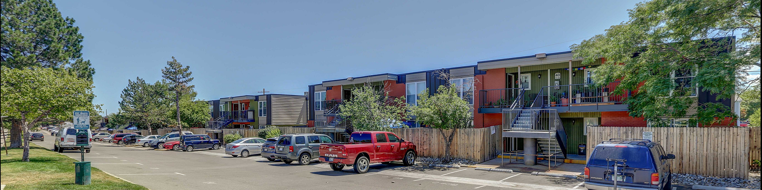 Vibrant apartment complex with ample parking and lush greenery on a sunny day.