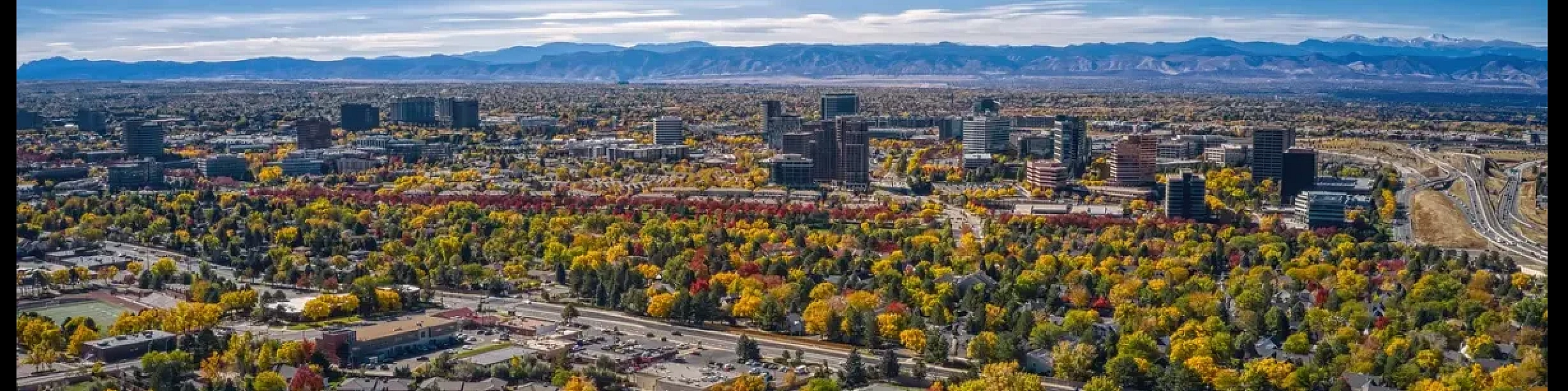 Vibrant aerial view of a bustling urban neighborhood with stunning mountain backdrop and colorful sunset skies.