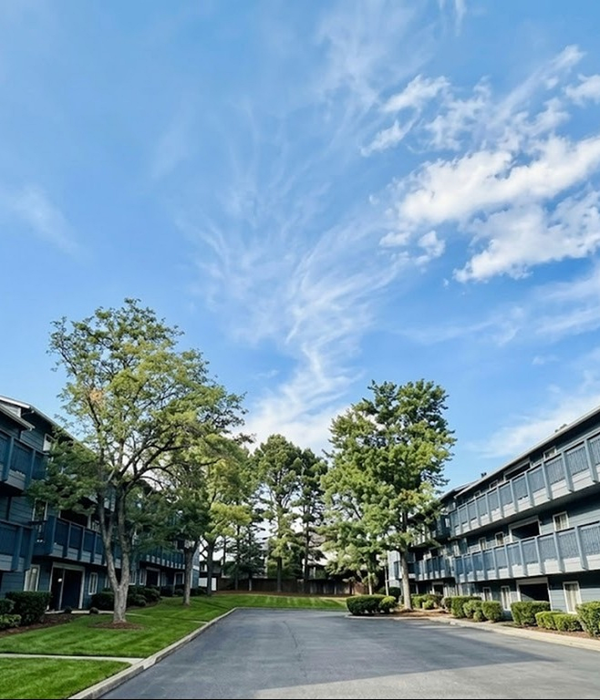 Bright apartment complex with lush greenery, offering modern living spaces and fresh air under a clear blue sky.